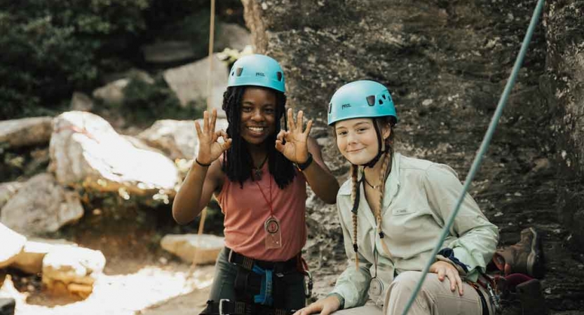 two young people wearing rock climbing gear smile at the camera on an outward bound expedition in north carolina